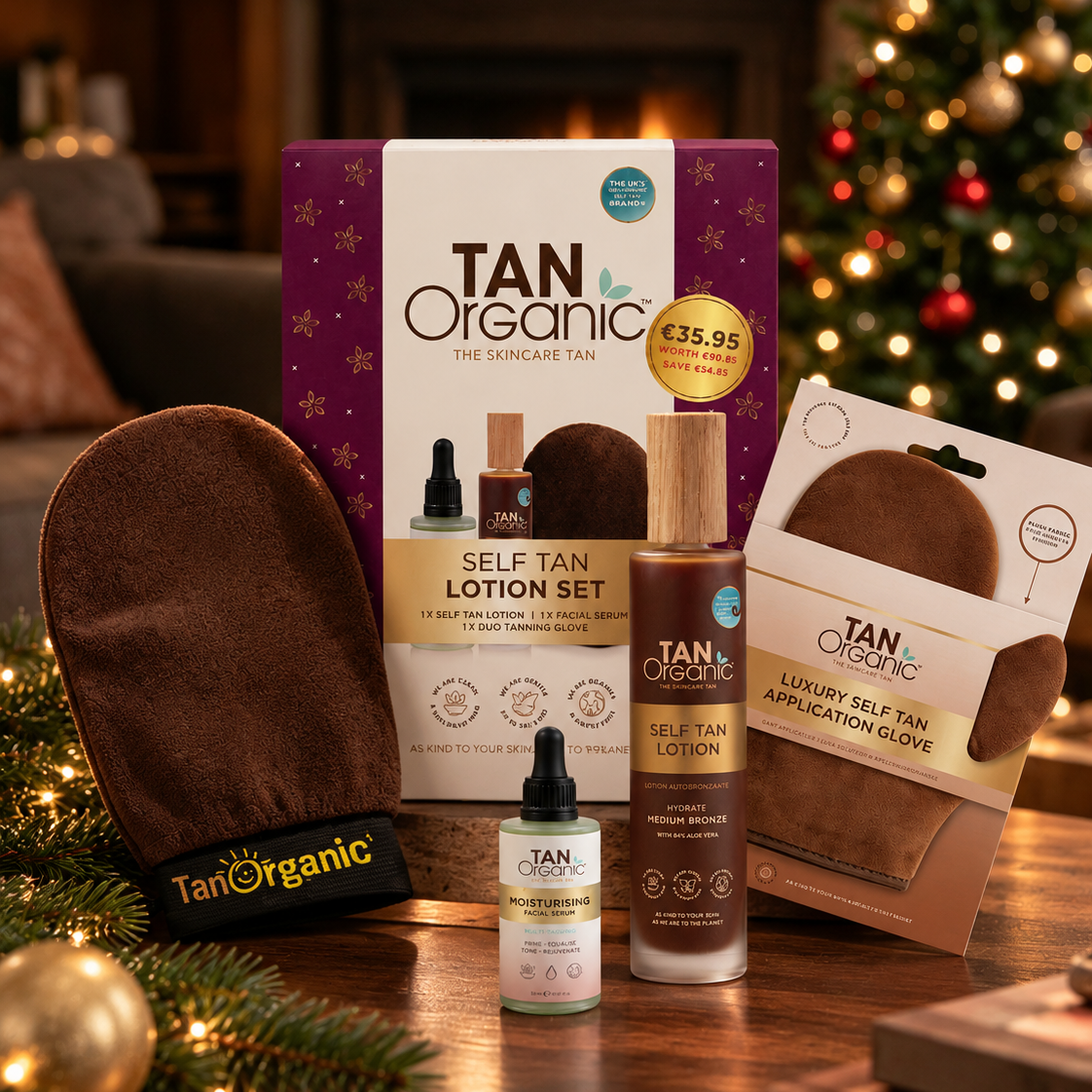 TanOrganic Self Tan Lotion Set with lotion, moisturising facial serum and tanning gloves beside a decorated Christmas tree.