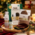 TanOrganic Self Tan Mousse Set with mousse, moisturising facial serum and tanning gloves on a wooden tray beside a Christmas tree.