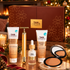 TanOrganic Star Gift set with Firming Gradual Self Tan Cream, Instant Tan, Facial Tan Serum, bronzer and gold facial tool beside a decorated Christmas tree.
